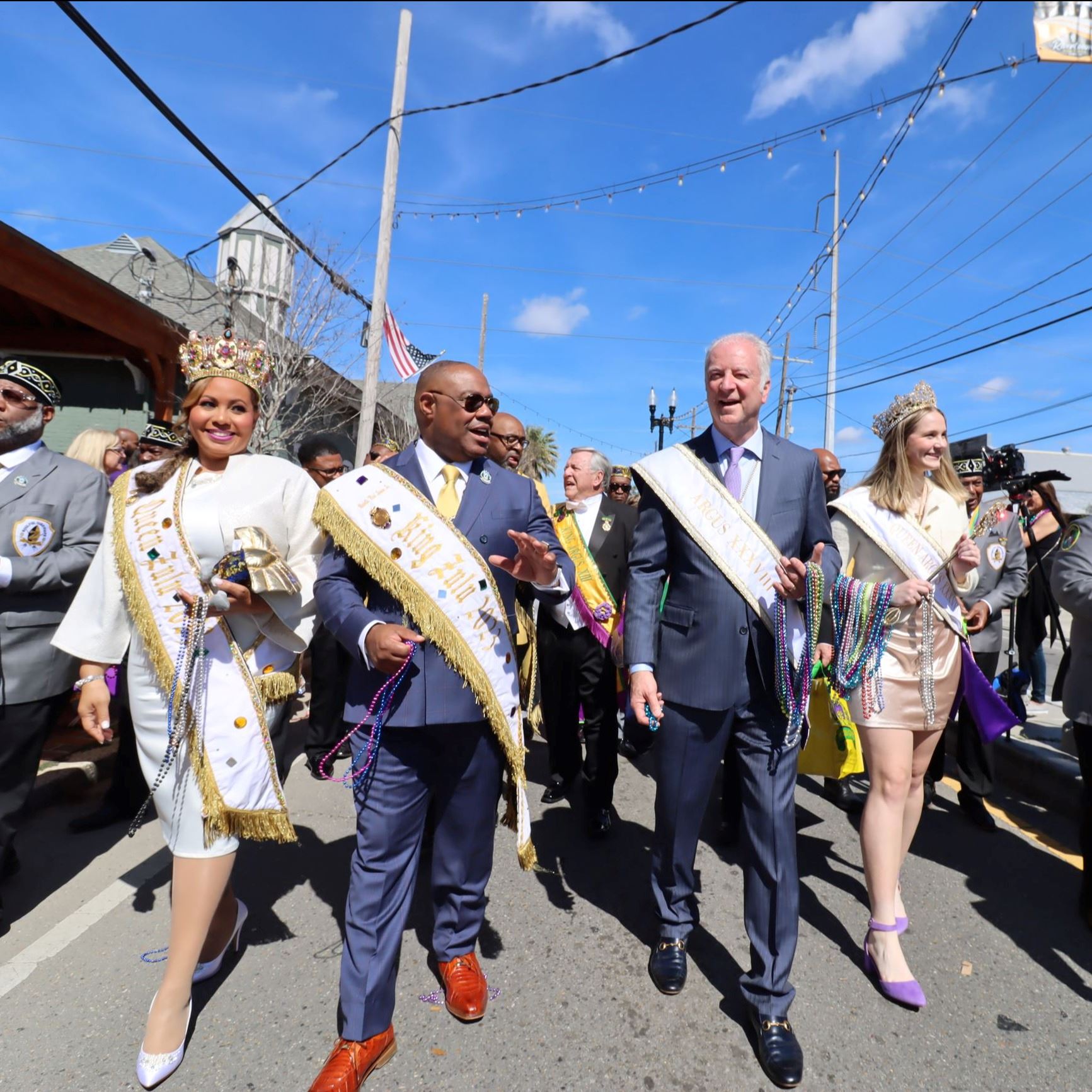 The queen and king of Argus and Zulu walking in the parade with the mayor and a group of people