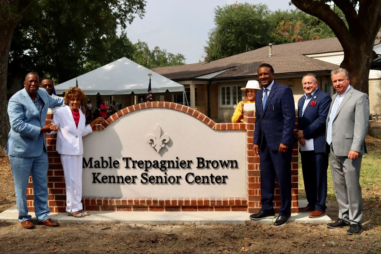 A group picture in front of the Mable Trepagnier Brown Kenner Senior Center sign and building
